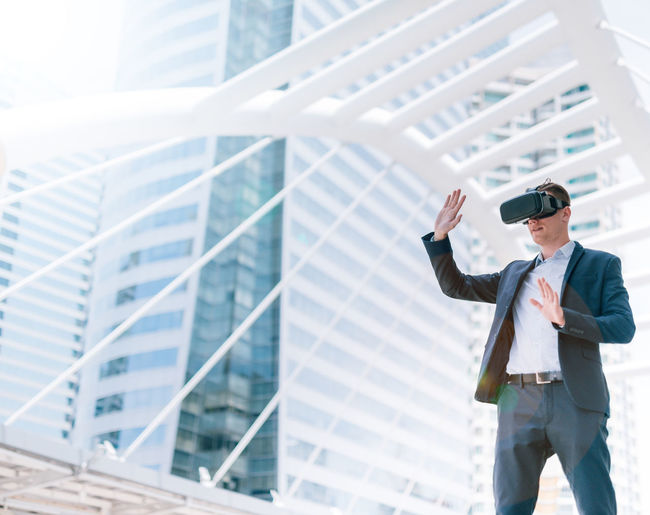 Businessman gesturing while using virtual reality stimulator against buildings in city