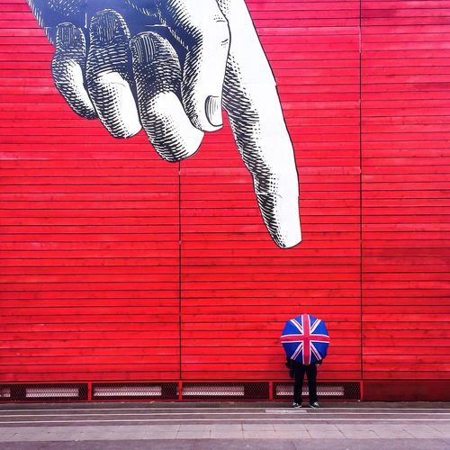 Person standing with umbrella against wall with mural