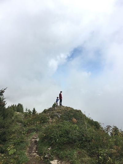 Low angle view of people standing on mountain against sky