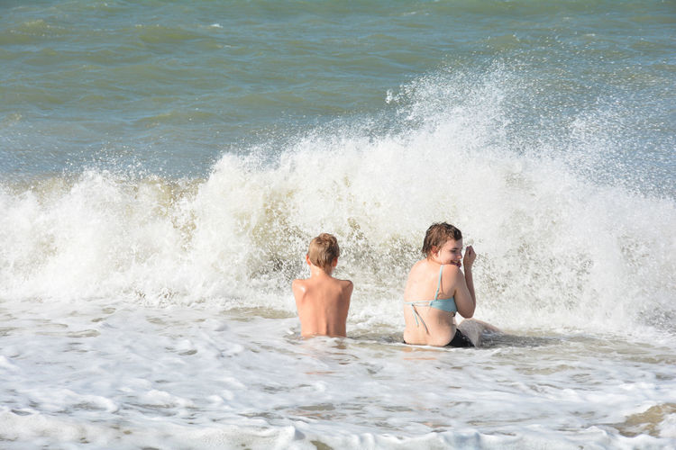 Full length of shirtless man splashing water in sea