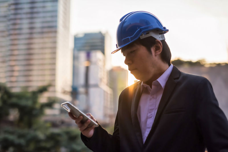 Man wearing hardhat using mobile phone outdoors