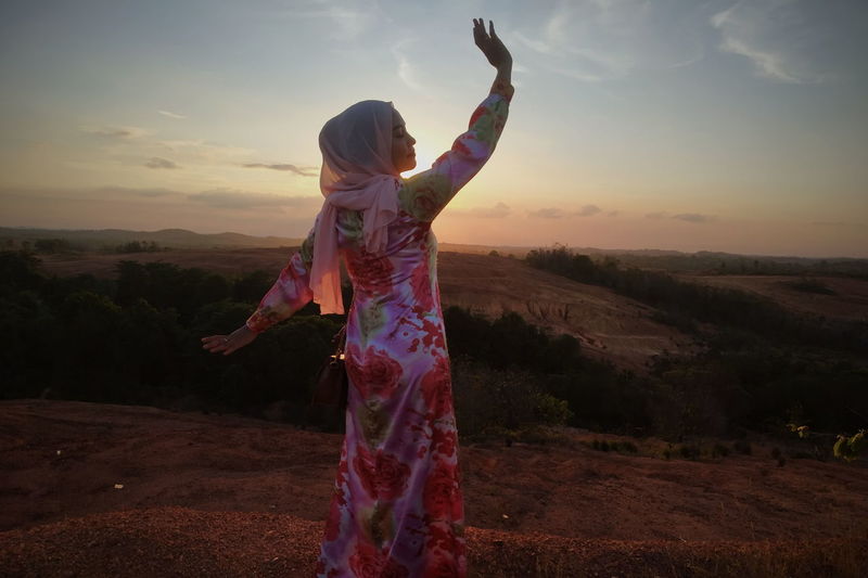 Full length of woman standing on landscape against sky during sunset