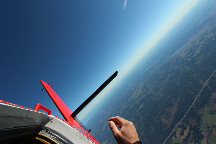 Cropped hand and airplane against clear blue sky