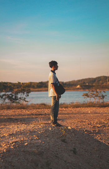 Man standing on lakeshore against sky during sunset