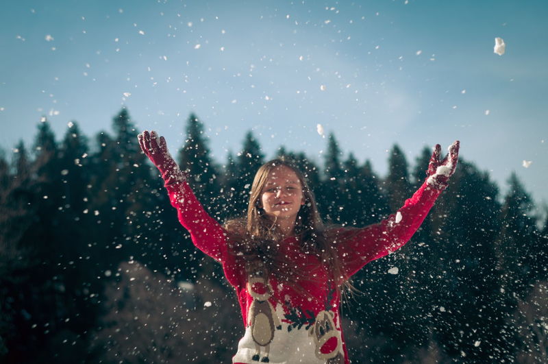 Smiling girl throwing snow while standing outdoors