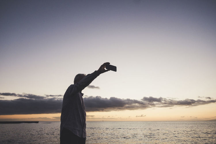 Man photographing from mobile phone at beach during sunset