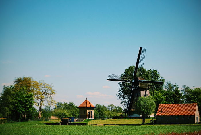 Traditional windmill on grassy field against clear sky