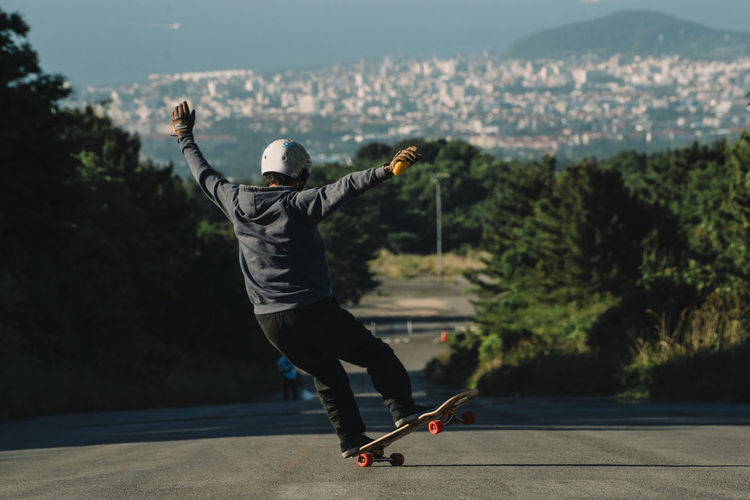 Rear view of man skateboarding on road against cityscape