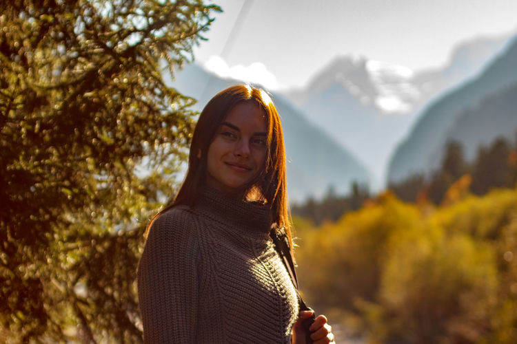 Portrait of woman standing by tree against mountain