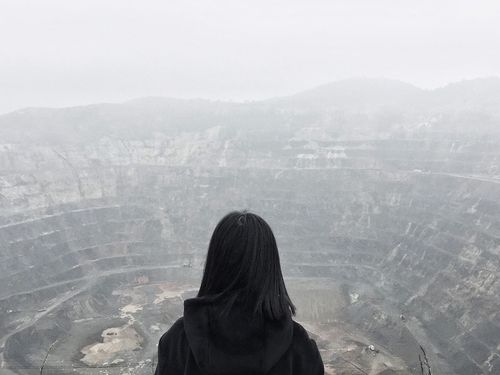 Rear view of woman standing against open-pit mine during foggy weather