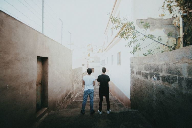Rear view of two friends standing on staircase amidst wall