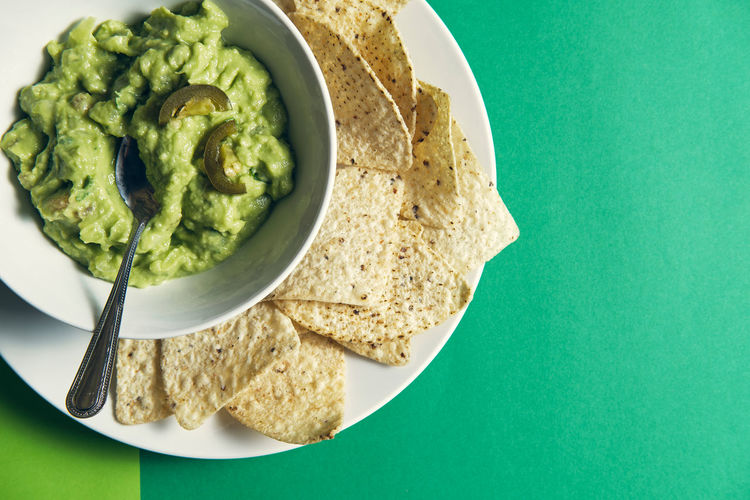 Guacamole sauce in a ceramic bowl on a green background