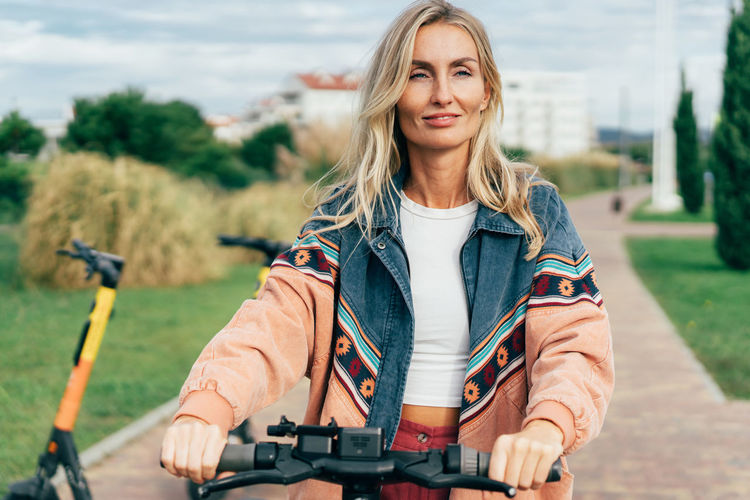 A young smiling woman rides a rented electric scooter.