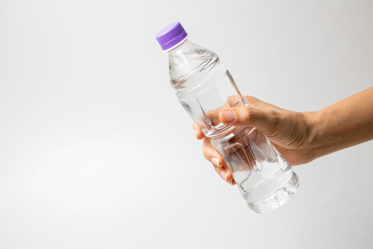 Hand holding glass bottle against white background