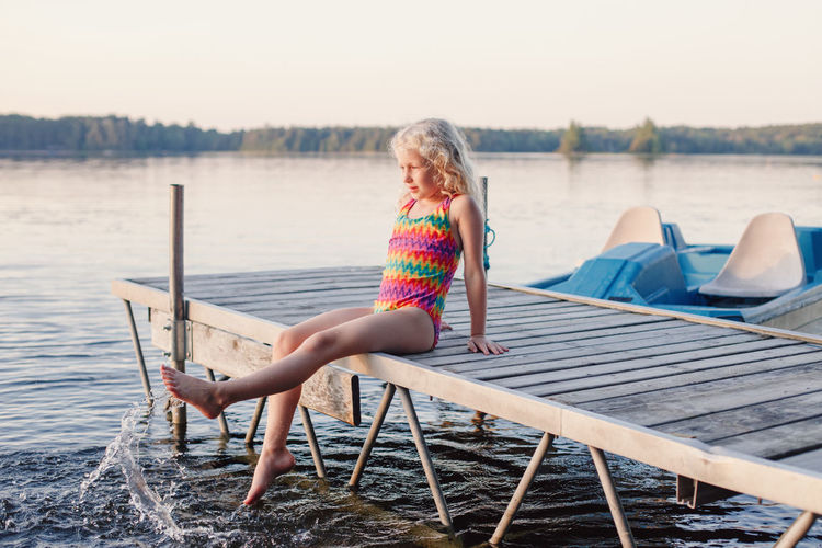 Girl sitting on pier over lake against sky