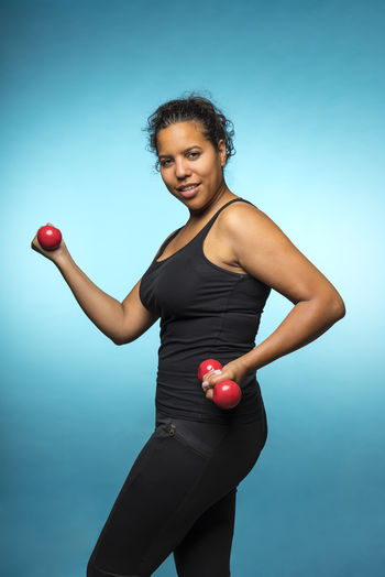Mixed raced young woman exercising with red 2 kg weights dumbbells isolated in blue
