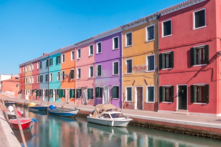 Boats moored in canal by buildings against sky