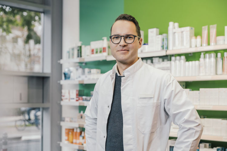 Smiling pharmacist wearing lab coat while standing in chemist shop