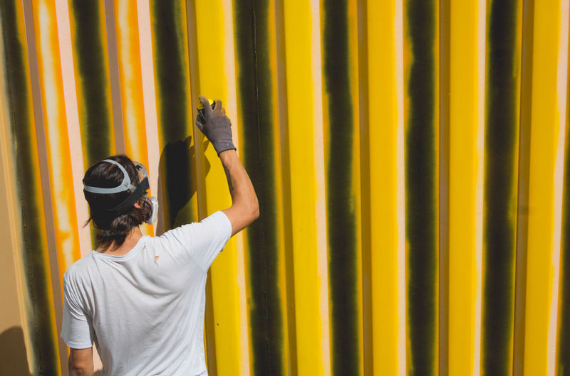 Young man, graffiti artist painting a wall in yellow
