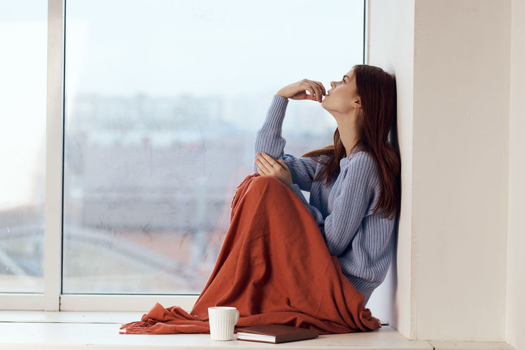 Side view of young woman drinking coffee from window