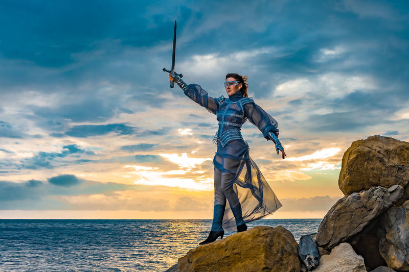 Rear view of man standing on rock by sea against sky during sunset