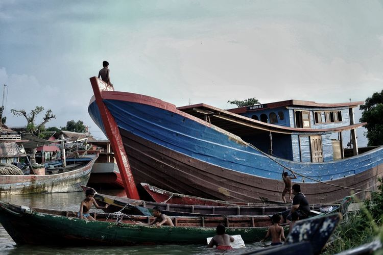 People on boat moored in water against sky
