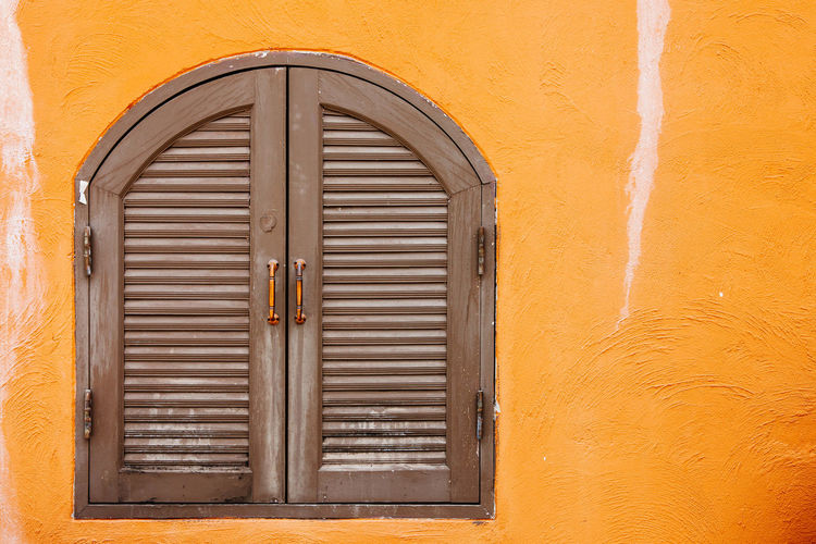 Old brown wooden window on the dirty orange concrete wall