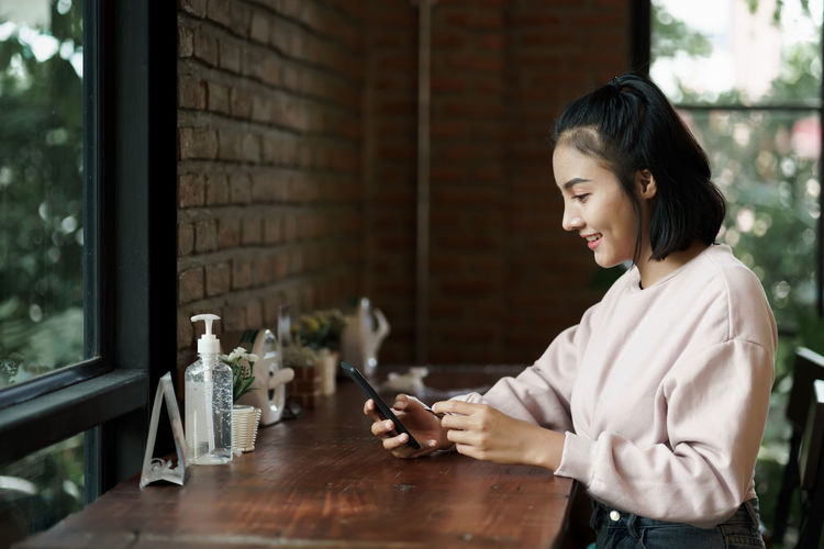 Young woman using smart phone on table at window