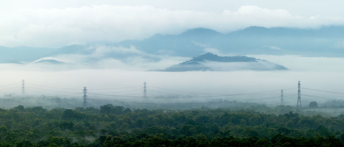 Tower in green forest and beautiful morning smooth fog.  high voltage power poles. mae moh, lampang.