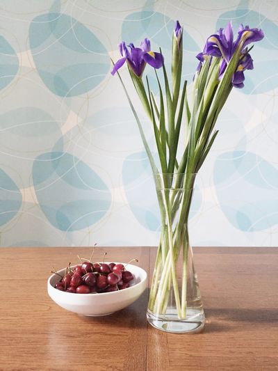 Iris flowers in vase by cherries on table