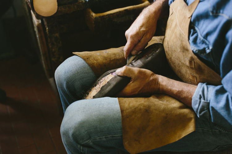 High angle midsection of craftsperson making shoe while sitting in workshop
