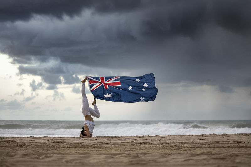 Woman holding flag while exercising on beach against sky