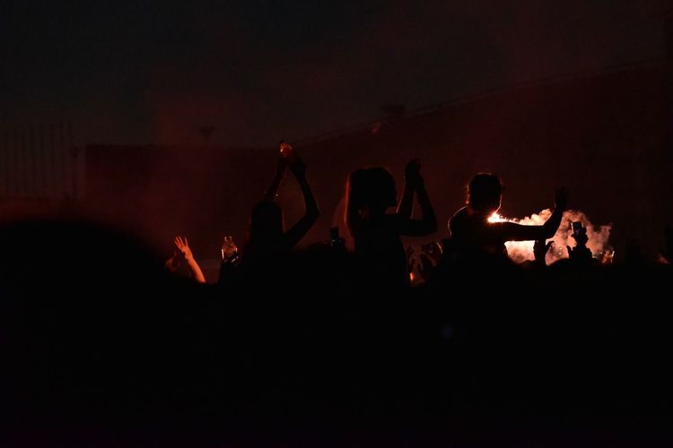 Silhouette people dancing against fire at night