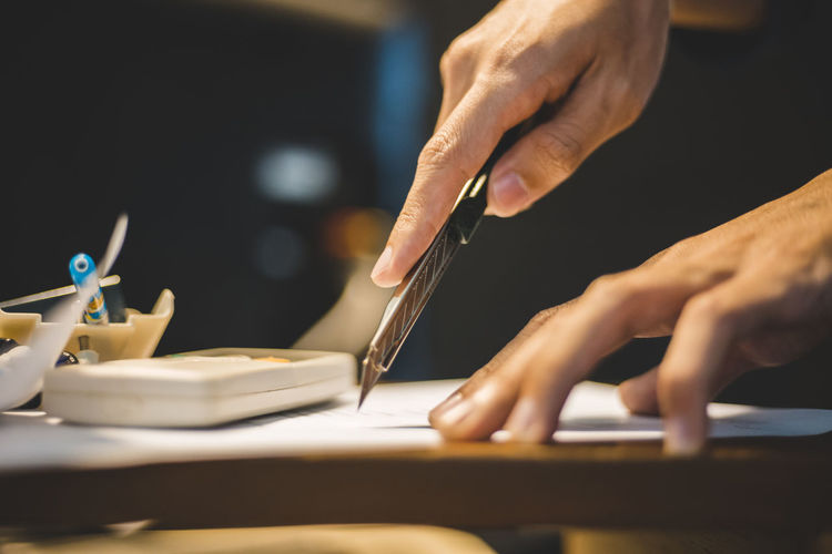 Cropped hands of man using blade on paper