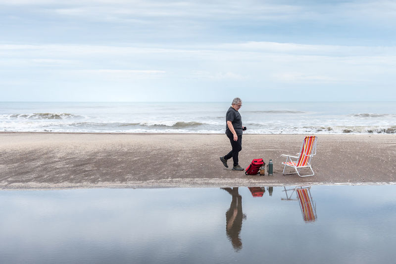 Mature man walking along the beach towards a set of mate next to a beach chair and in behind the sea