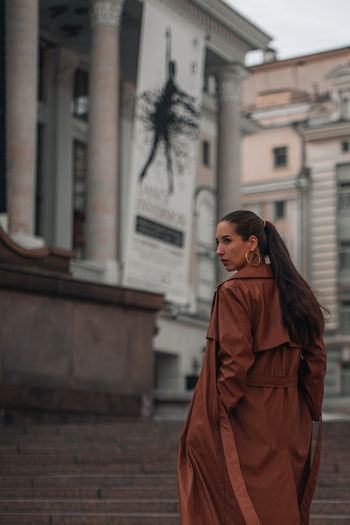 Stylish young brunette woman in fashionable long brown leather coat. autumn street style. casual