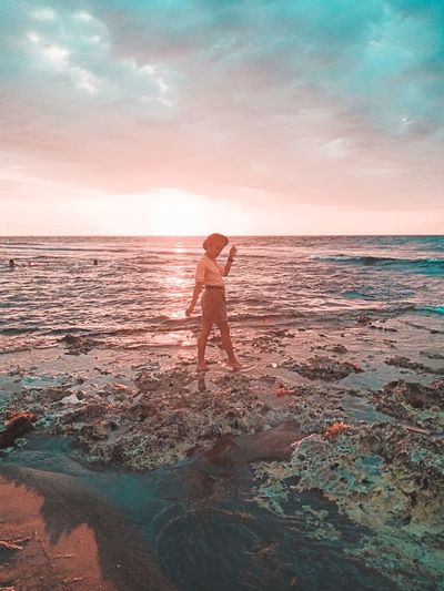 Man standing at beach against sky during sunset