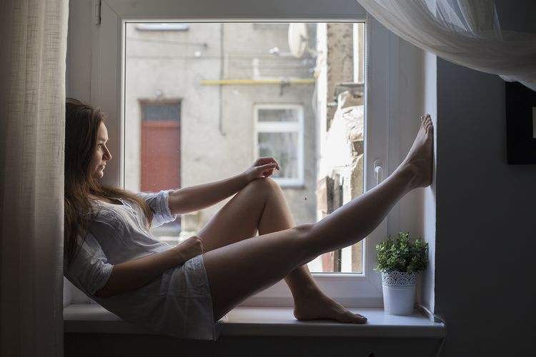 Side view of woman sitting on window sill at home