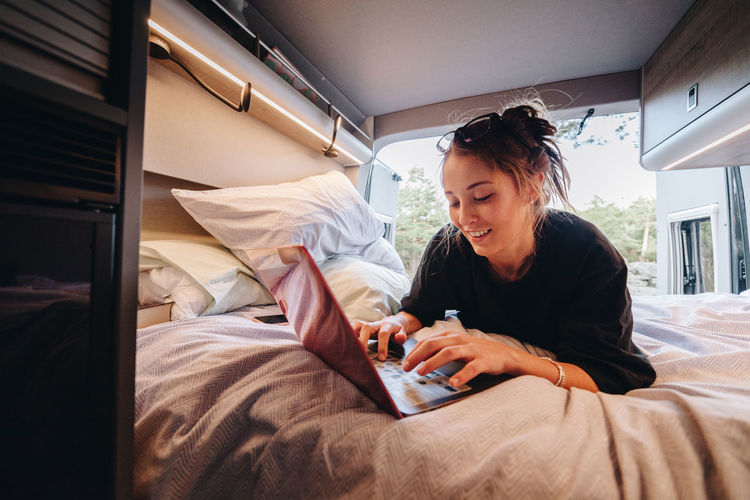 Young woman using mobile phone while sitting on bed at home