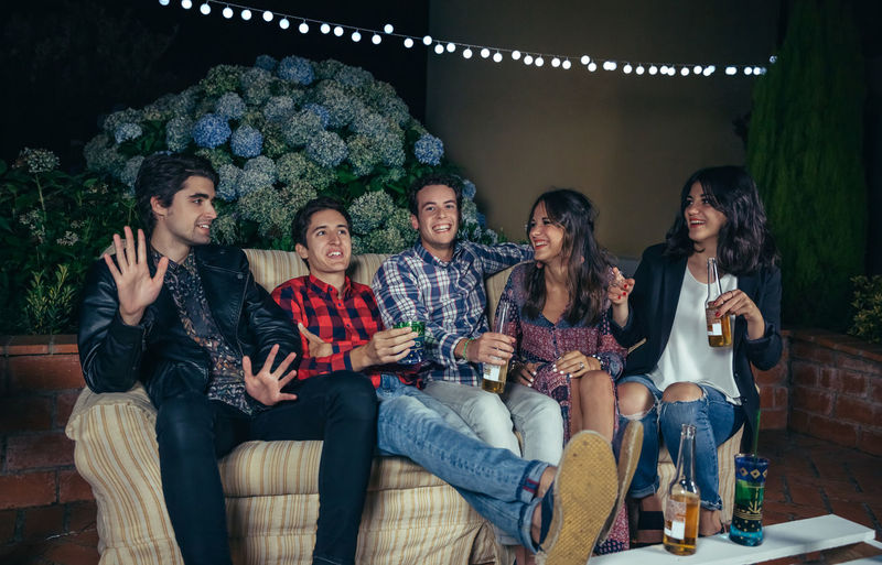 Cheerful friends talking while sitting on sofa at patio during night