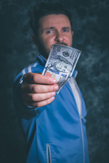 Portrait of man holding american one hundred dollar bill against wall