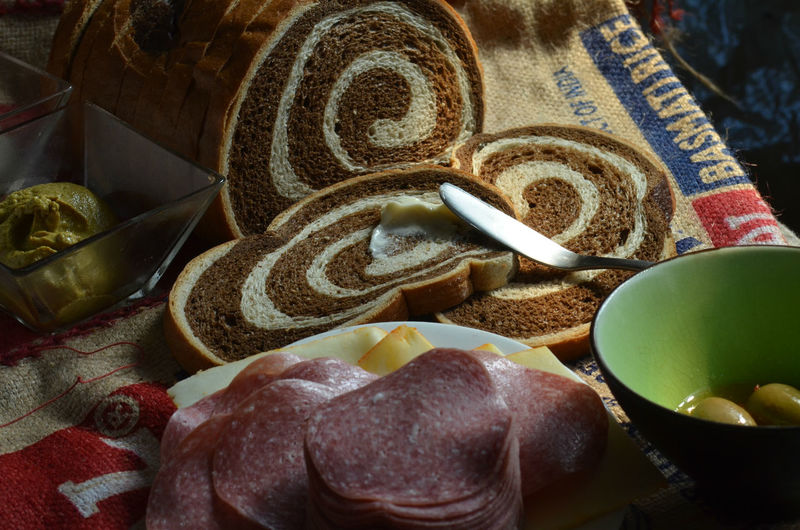 Close-up of marble rye bread by salami and green olives in bowl on table
