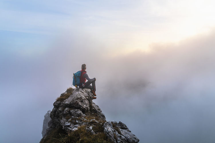 Pensive male hiker sitting on mountain peak during sunrise at bergamasque alps, italy