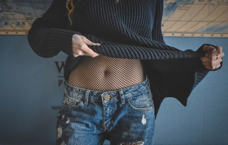 Midsection of woman undressing while standing against wall
