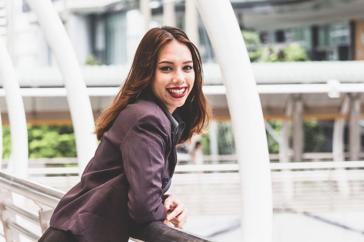 Portrait of smiling young businesswoman standing on elevated walkway 