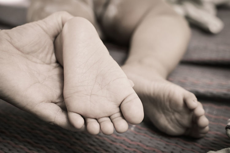 Cropped hand holding baby feet on bed