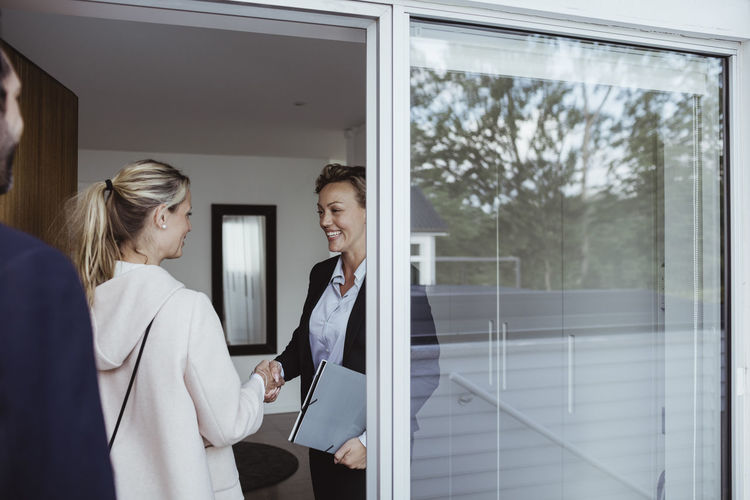 Smiling female real estate agent greeting couple in new house