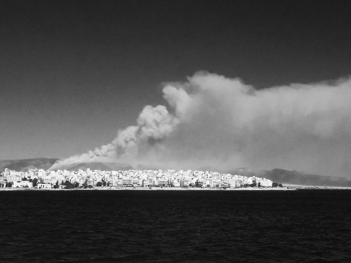 Smoke emitting from city by sea against sky
