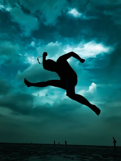 Silhouette man jumping against cloudy sky