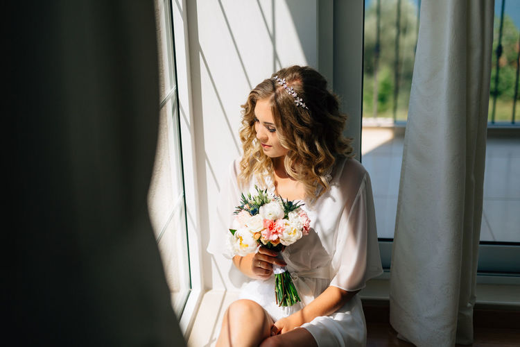 Woman holding flower bouquet sitting by window